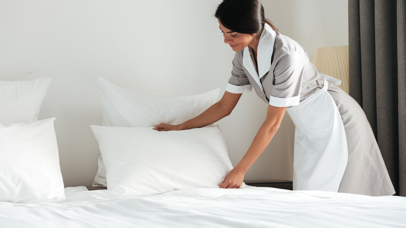 A woman placing pillows on top of a bed